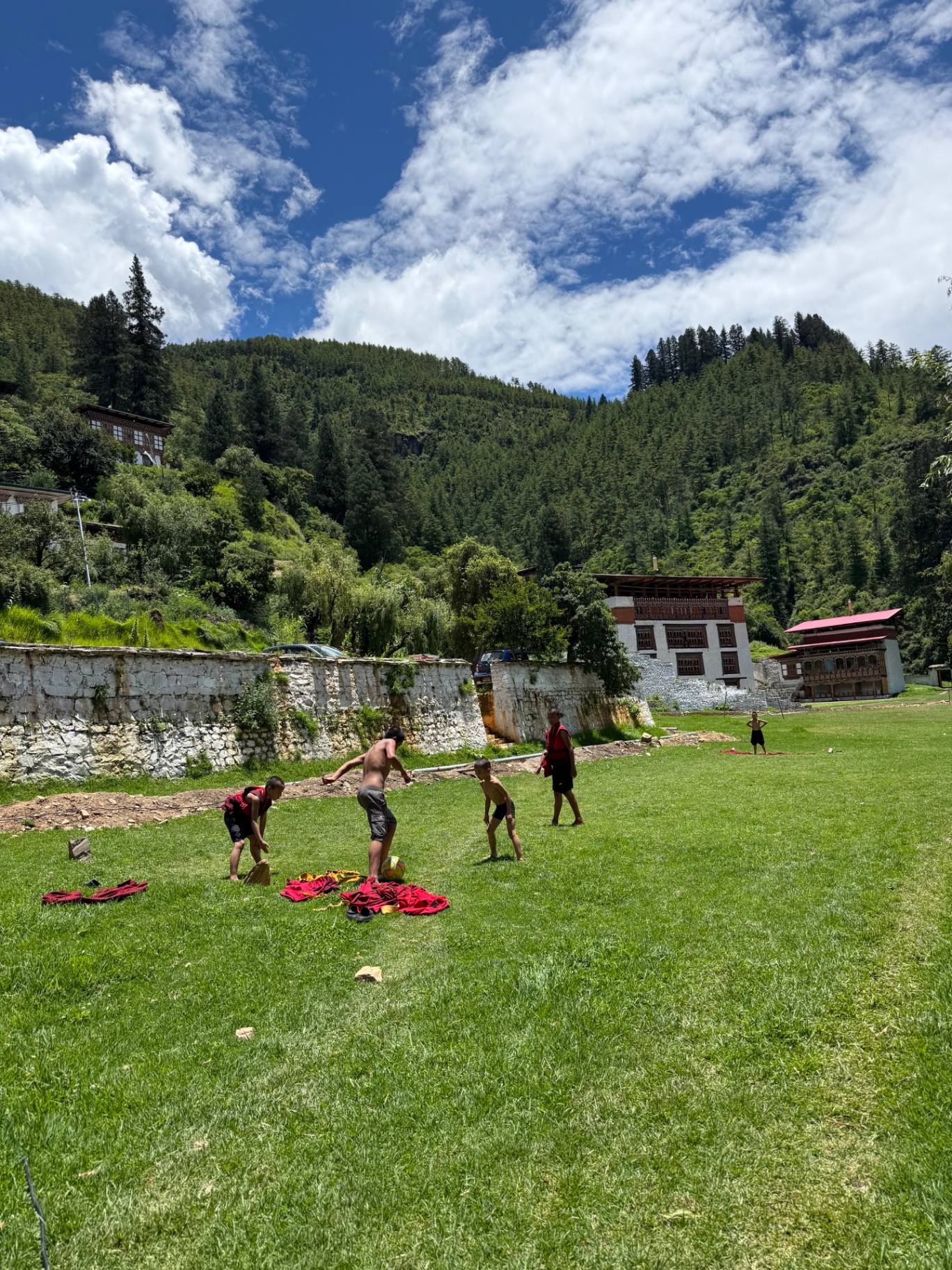 Young monks playing football on a grassy field below forested hills