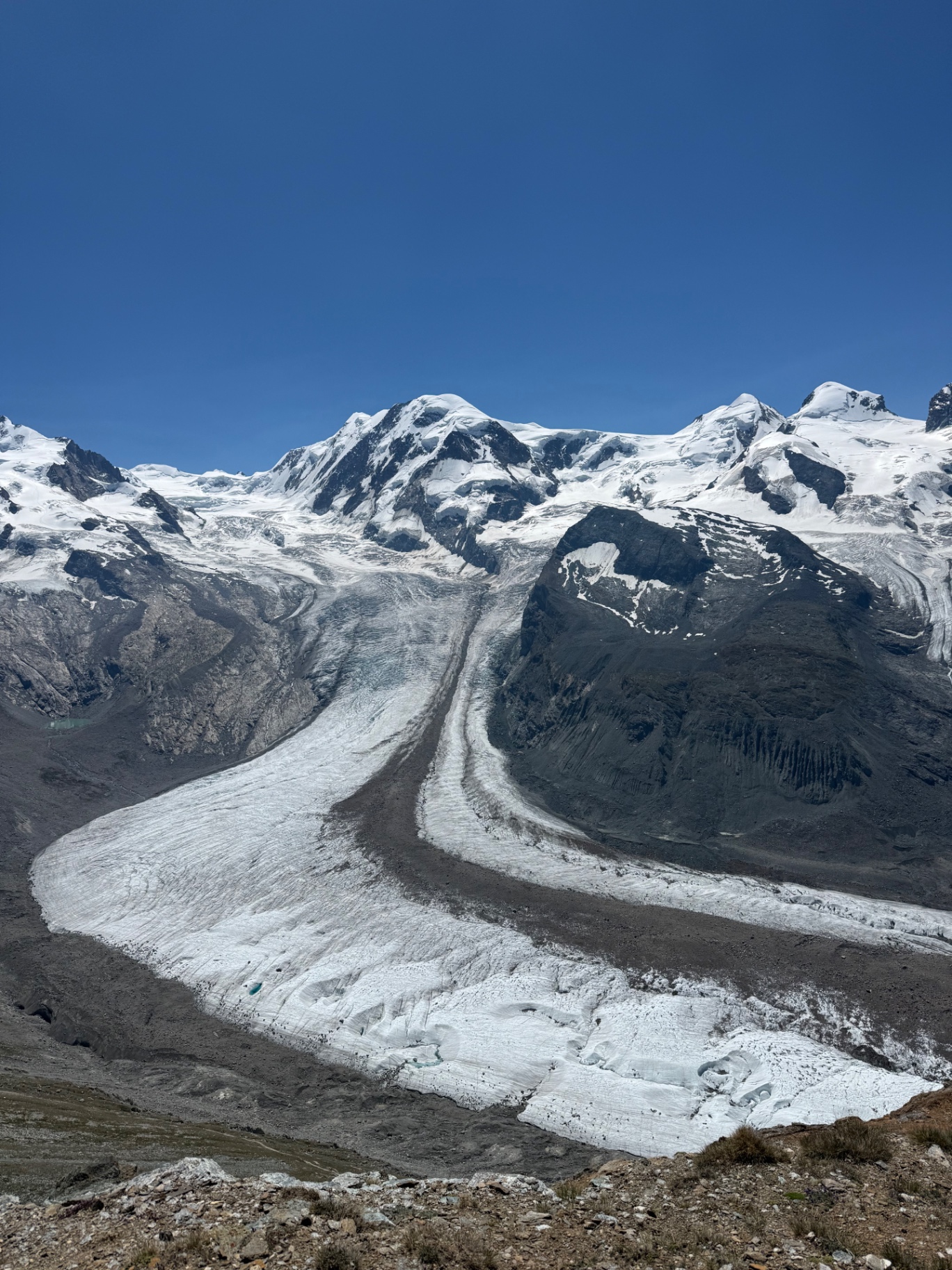 A wide glacier curving down between snowy peaks under a deep blue sky