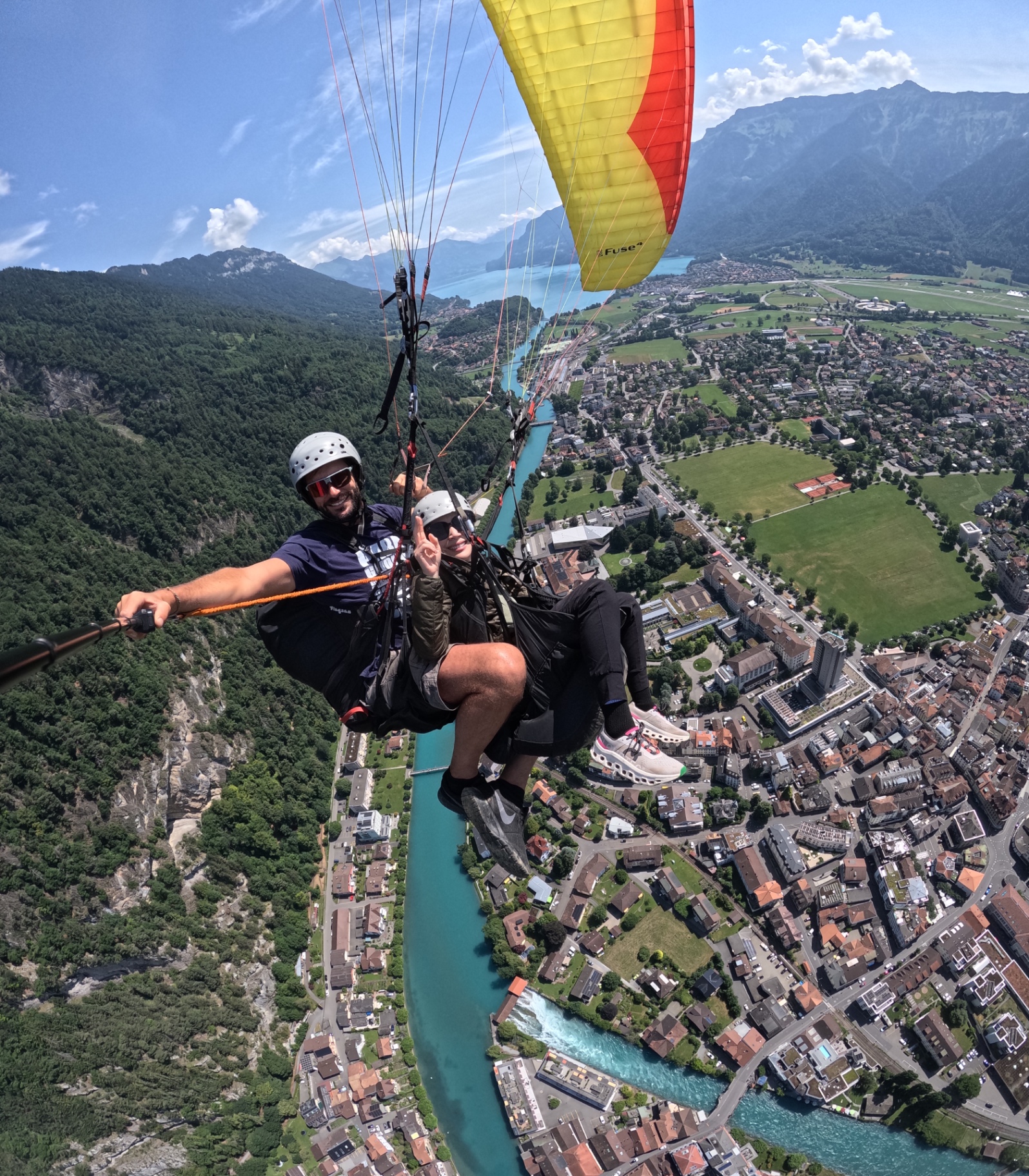 Tandem paragliding high above a turquoise river, a town and lakes between mountains