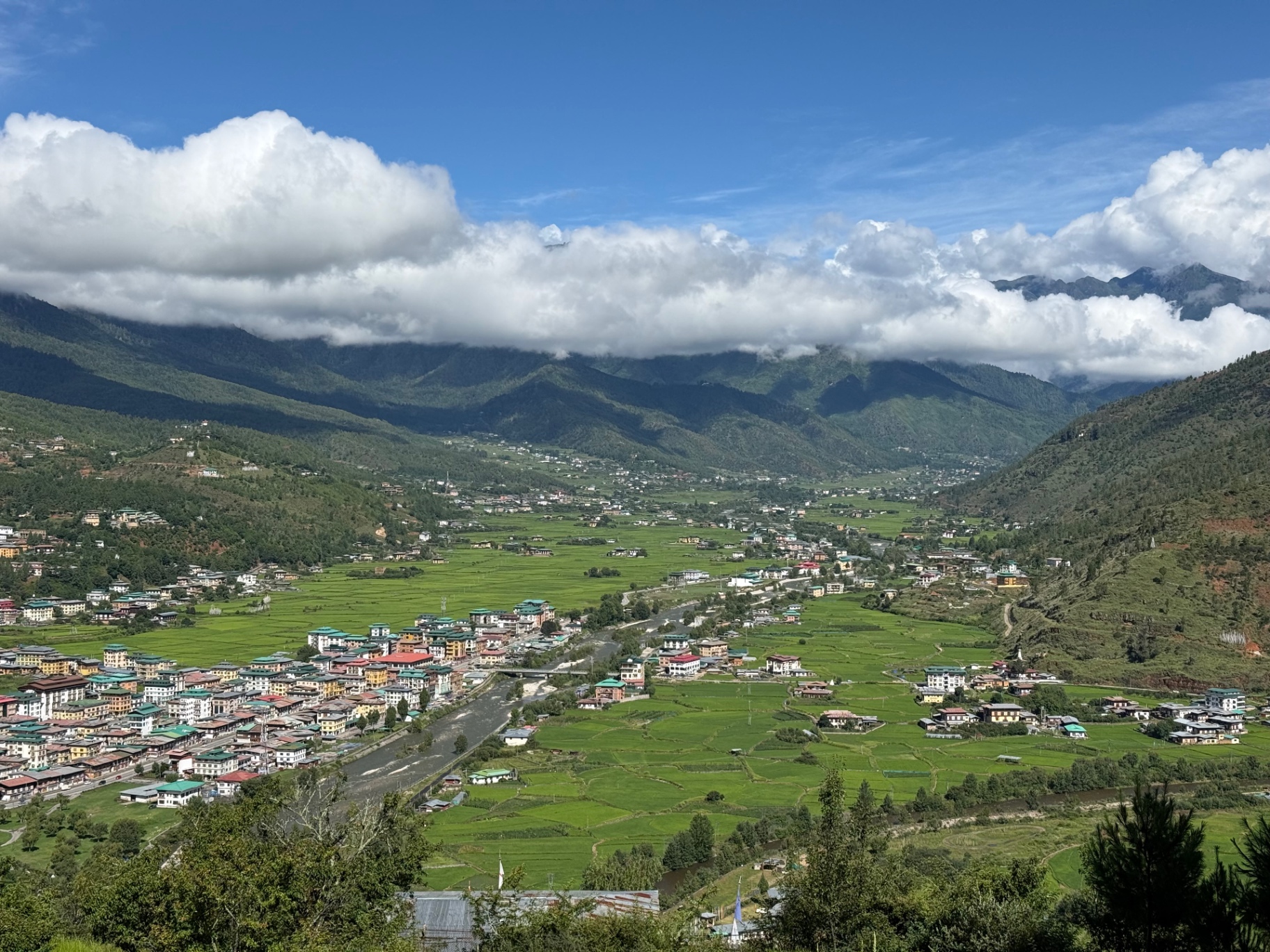 A green valley with a river, rice fields and a small town under low white clouds