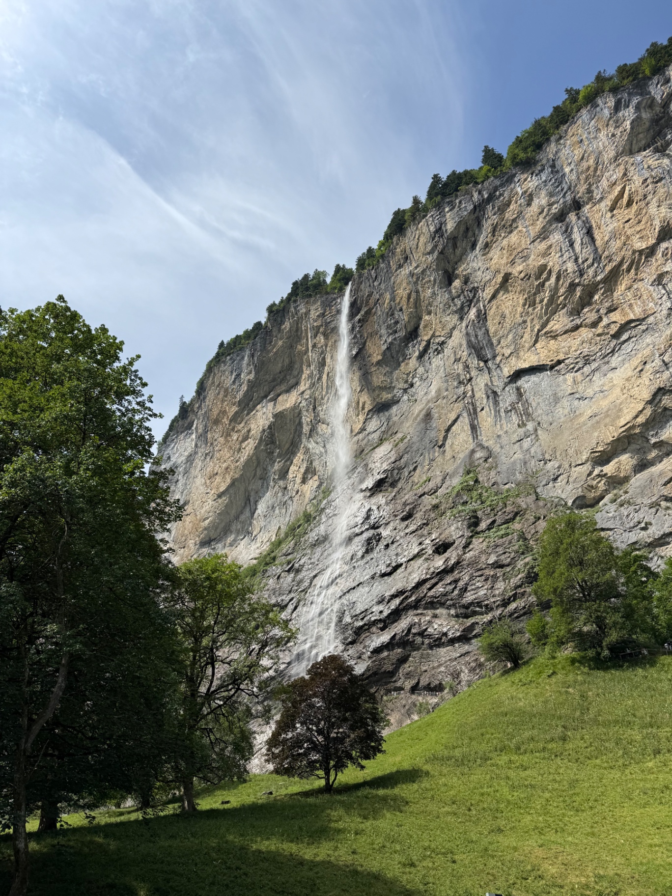 A tall waterfall dropping down a sheer cliff above a green meadow