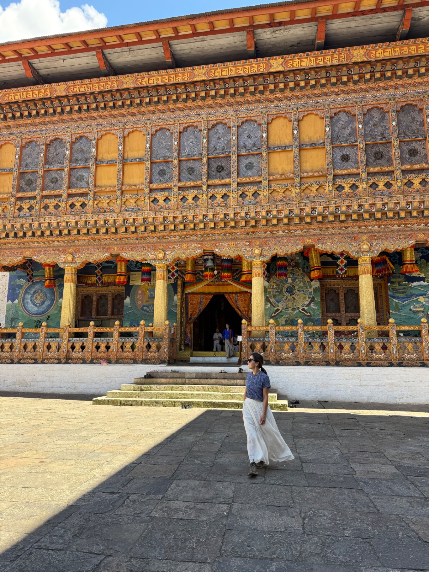 Walking across a sunny stone courtyard in front of a richly painted Bhutanese dzong